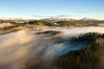 Aerial view of a small distant village houses on hill top in fall foggy mountains at sunrise.