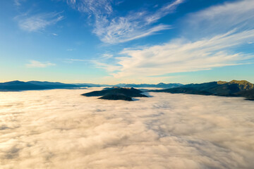 Aerial view of yellow sunset over white puffy clouds with distant mountains on horizon.
