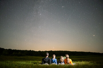 Parents and their kids resting in night field observing dark sky with many bright stars. © bilanol