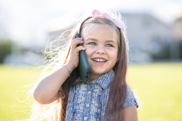 Pretty happy child girl talking on mobile phone smiling outdoors in summer.