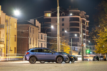 Blue car parked on brightly illuminated city street at night. © bilanol