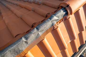 Closeup of yellow ceramic roofing ridge tiles on top of residential building roof under construction. - obrazy, fototapety, plakaty