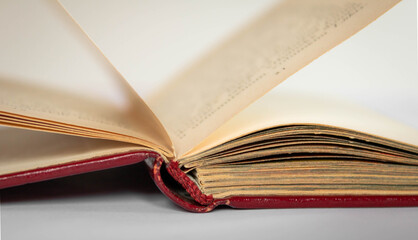 Close up of an open antique book with red leather covers and pages standing on white background, golden binding