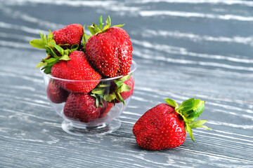 Strawberries in a glass bowl on a gray wooden natural background, a copy space