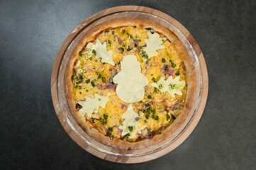 New year style pizza served on wooden board. Kids food. Pizza decorated with holiday Christmas cheese trees. Served with pesto sauce. Dark stone background. Pizza with cheesy snowman silhouette on top