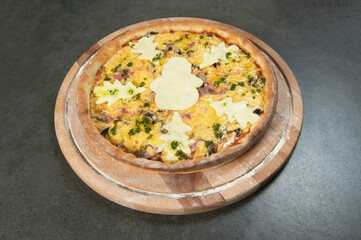 Meat New year style pizza with pesto sauce served on wooden board. Kids food. Pizza decorated with holiday Christmas cheese trees. Dark stone background. Pizza with cheesy snowman silhouette on top
