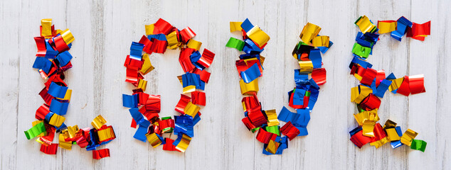 Word LOVE made of colored bright confetti on a light wooden background. View from above. Banner