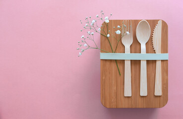 Set of cutlery (fork, spoon, knife) made of wood or bamboo, bamboo reusable lunch box. Zero waste concept. Pink background. Top view