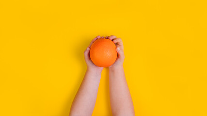 Fototapeta na wymiar Hands of little girl with orange fruit on orange background. Top view. Banner. Copy space