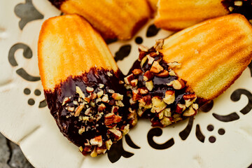 close up of madeleine French cookies dipped in chocolate and chopped nuts served on white fancy cutwork metal plate