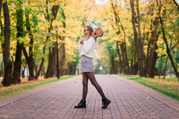 Fototapeta premium A young woman is sitting on the bench in the park and playing ukulele
