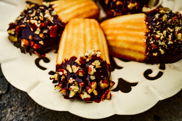 Close up of madeleines dipped in chocolate and chopped nuts served on fancy metal cutwork dessert plate.