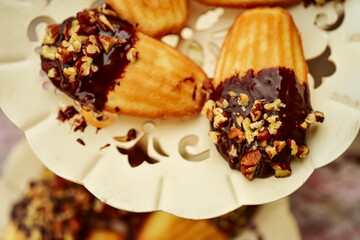Close up of madeleines dipped in chocolate and chopped nuts served on fancy metal cutwork dessert plate.
