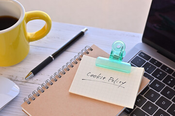 There's a note pinned to a clip on my desk. It says something like Cookie Policy on it. There's a coffee and a pen and a laptop nearby.