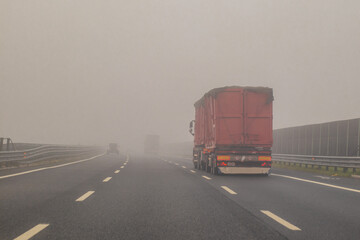 Truck or lorries and one van overtaking at a dangerous time with thick fog on a motorway in italy, europe.