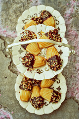 fancy three tier dessert plate filled with madeleine cookies dipped in chocolate and chopped nuts