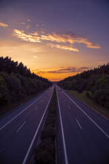 Highway through the forest with empty lanes at sunset
