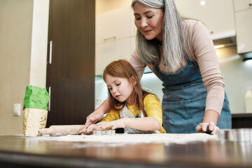 Grandmother helping little granddaughter during cookies cutting