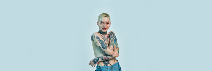 Tattoo and piercing. A white tattoed pierced woman standing topless with her hands crossed on her...