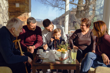 Small caucasian boy is eating french fries potato chips at restaurant or at home in day while his family is watching - little kid having snack with his mother, father grandmother and grandfather