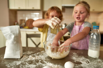 Two little children, boy and girl in aprons helping each other whille preparing dough for cookies...