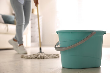Plastic bucket and woman mopping floor in living room, closeup. Cleaning supplies