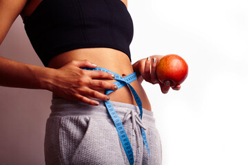 woman measuring waist with tape on knot, african tan isolated on white background, holding red apple