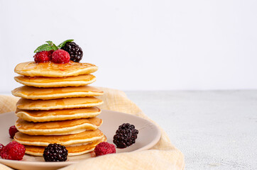 Homemade classic American pancakes with fresh raspberries, blackberries, honey and mint leaves, on a light background. Copy space, flat lay. Healthy summer breakfast. Close-up. View from above.