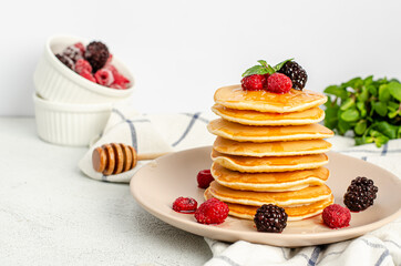 Homemade classic American pancakes with fresh raspberries, blackberries, honey and mint leaves on a light background. Copy space, flat lay, space for text. Healthy summer breakfast. Close-up.