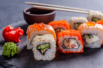 Seth sushi roll with salmon, eel, tuna, avocado, cucumber, Philadelphia cream cheese, tobik caviar, on a black slate board, dark background. Sushi menu. Japanese food. Close-up.