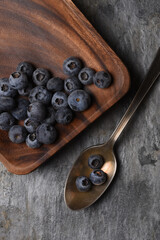 Flat lay still life of fresh blueberries in an antique spoon next to a wood plate with more fruit. Vertical with copy space.