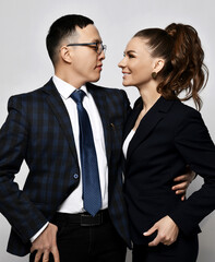 Young smiling couple man and woman business partners coworkers in official clothing standing hugging and looking at each other over light wall background. Teamwork, cooperation, business