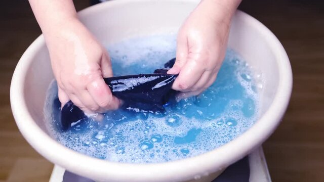 woman washes with her hands blue men's panties in a basin, knitted underwear, clean clothes concept, scandal in the Russian Federal Security Service