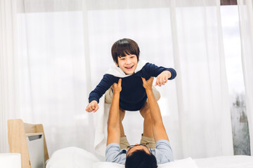 Fototapeta na wymiar Portrait of enjoy happy love asian family father carrying little asian boy son smiling playing superhero and having fun moments good time on bed at home