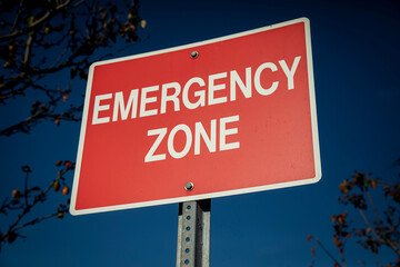 Red sign with white letters stating Emergency Zone against a blue sky