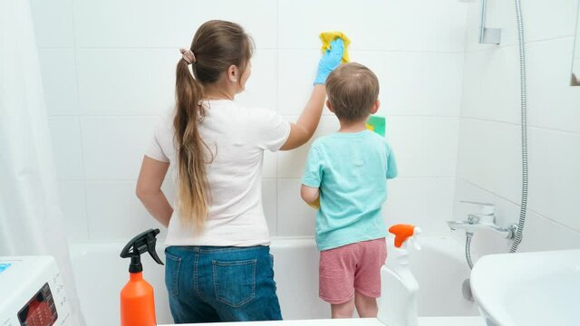 Little toddler boy with young mother washing and cleaning tile walls in bathroom while doing housework and home cleanup