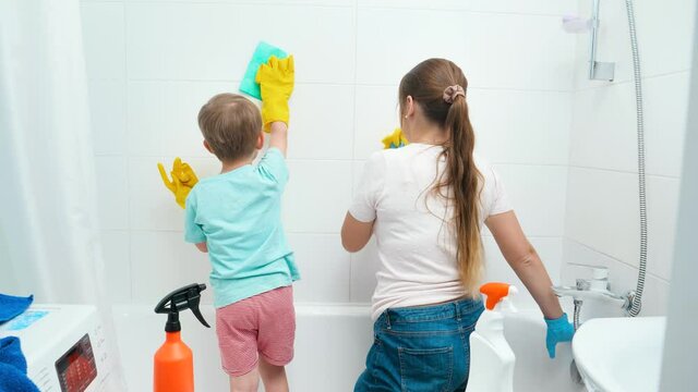 Young mother with her little son having fun and smiling while washing walls in bathroom. Family enjoying housework and home cleanup