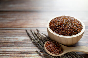 Red rice in wooden bowl and wooden spoon on wooden table.
