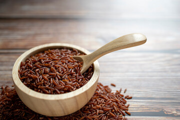 Red rice in wooden bowl with wooden spoon in bowl all on wooden table.