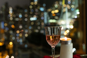 glass red wine and candles on table, twinkling blurred city night lights in background, romantic concept for lovers and valentine