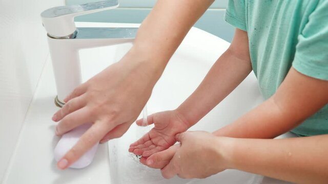 CLoseup of mother teaching and showing her little son how to wash hands. Child using antibacterial soap while washing hands in bathroom