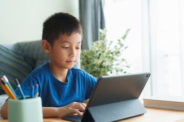 Asian boy is studying online via the internet on tablet while sitting in the living room in morning - 403732783