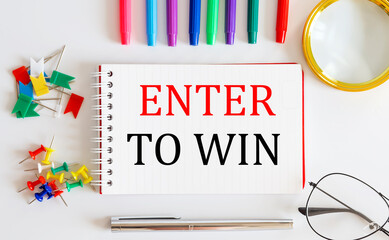 Notebook with ENTER TO WIN word with office tools on the white table.