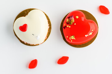 .A cake in heart shape. Two heart shaped mousse cupcakes white and red  and candy on a white background. Valentine's Day.