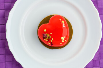 .A cake in heart shape. One heart-shaped mousse cupcake on a plate on a purple background. Valentine's Day.