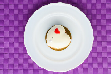 A cake in heart shape. One heart-shaped mousse cupcake on a plate on a purple background. Valentine's Day.