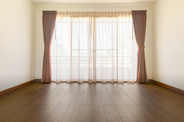 The empty room has wooden floors and curtains.