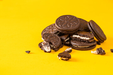 Chocolate sandwich cookies with vanilla cream filling  and  cookies crumbs on yellow background.