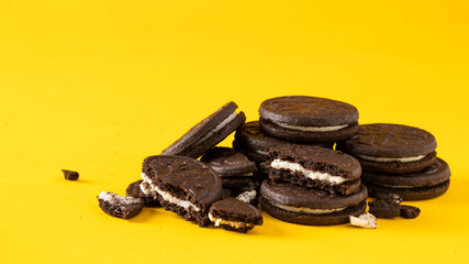Chocolate sandwich cookies with vanilla cream filling  and  cookies crumbs on yellow background.