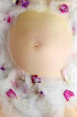 Pregnant woman and her belly in milk bath with flowers. Czech Republic. Europe.